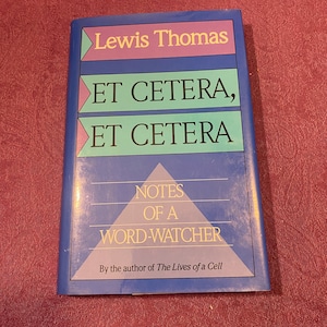 Pode incluir: Um livro azul com o título "Et Cetera, Et Cetera: Notes of a Word-Watcher" de Lewis Thomas. O livro é do autor de "The Lives of a Cell".
