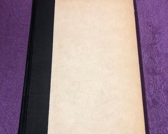 Op de afbeelding: Een vintage hardback boek met een zwarte rug en een crèmekleurige omslag. De omslag heeft een textuur.