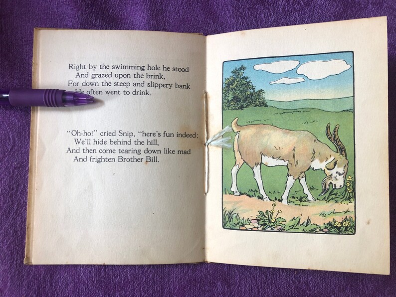 May include: An open book with a brown goat illustration on the right page. The goat is walking on a path in a green field. The left page has text that reads 'Right by the swimming hole he stood And grazed upon the brink. For down the steep and slippery bank He often went to drink. 'Oh-ho!' cried Snip, 'here's fun indeed: We'll hide behind the hill, And then come tearing down like mad And frighten Brother Bill.'