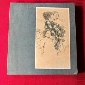 Op de afbeelding: Een lichtblauw boek met een rechthoekige illustratie van drie geschetste figuren. De illustratie staat op een crèmekleurige achtergrond. Het boek ligt op een rode ondergrond.