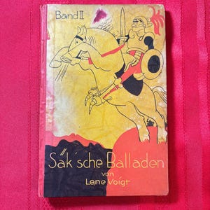 Puede incluir: Portada de libro vintage con un caballero a caballo, en amarillo, negro y rojo. El título "Saksche Balladen" se muestra en letras blancas sobre un fondo negro y rojo. El libro se titula "Band I".