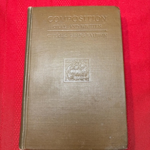 May include: A brown book titled "Composition Oral and Written" by Charles Sears Baldwin. The book has a gold embossed image of a ship on the front cover.