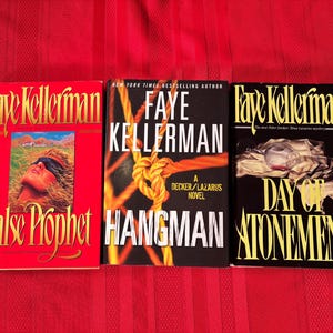Könnte beinhalten: Drei Bücher von Faye Kellerman werden gezeigt. Die Titel sind "False Prophet", "Hangman" und "Day of Atonement". Die Cover sind in Rot, Schwarz und Gelb gehalten und enthalten Illustrationen und Text. Die Bücher liegen auf einer roten Oberfläche.