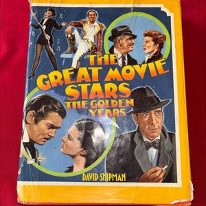May include: A vintage book titled "The Great Movie Stars: The Golden Years" with a yellow border. The cover features illustrations of classic Hollywood actors and actresses. The author's name, David Shipman, is printed at the bottom.