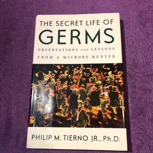 Peut inclure: Un livre intitulé "The Secret Life of Germs: Observations and Lessons from a Microbe Hunter" par Philip M. Tierno Jr., Ph.D. La couverture présente une illustration colorée d'une foule de personnes.