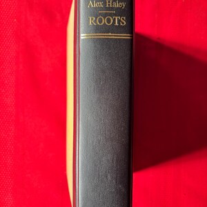 May include: A black hardcover book with gold lettering on the spine. The title is "Roots" by Alex Haley. The book is published by Doubleday.