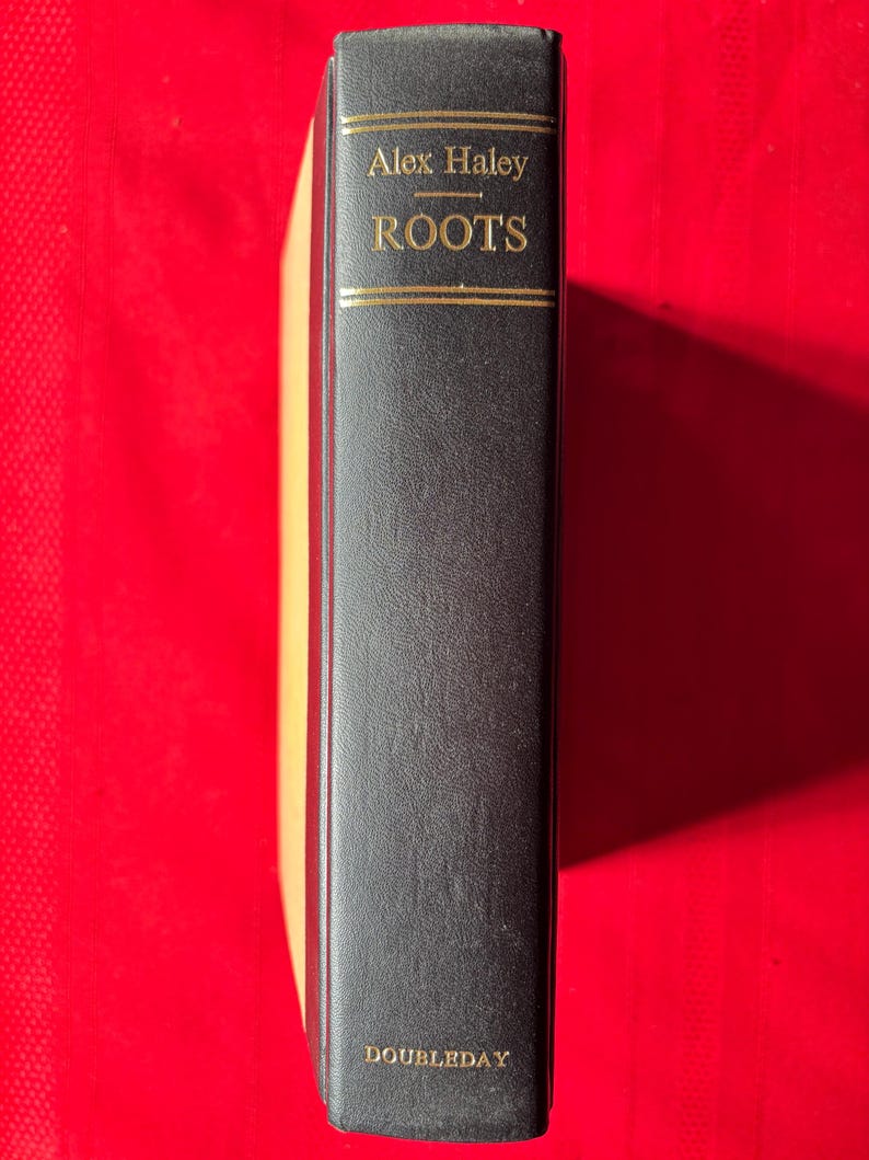 May include: A black hardcover book with gold lettering on the spine. The title is "Roots" by Alex Haley. The book is published by Doubleday.