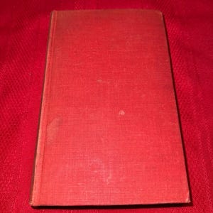 May include: A vintage hardcover book with a textured, red cover. The book is rectangular and appears to be closed, with a slightly worn appearance. The cover has a subtle pattern and a darker spine.