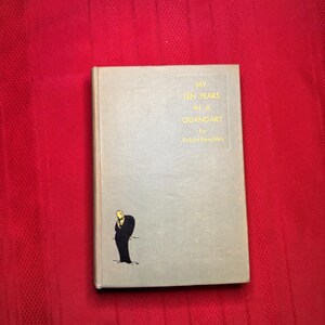 May include: A hardcover book titled "My Ten Years in a Quandary" by Robert Benchley. The book has a light gray cover with gold lettering and a small illustration of a man in a black coat. The book is set against a red background.
