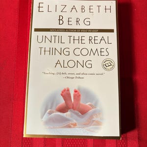 May include: A book cover with a gold background and a white title that reads "Until the Real Thing Comes Along" by Elizabeth Berg. The book cover features a photo of a baby's feet.