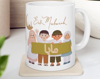 May include: White ceramic mug with a handle, featuring a cartoon illustration of four children holding a green banner with the word "Mama" written in Arabic script. The text "Eid Mubarak" is written in cursive above the children.