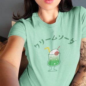 May include: A green t-shirt with a cartoon illustration of a green and white cream soda with a cherry on top and a straw. The text "クリームソーダ" is printed in black above the illustration.