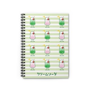 Puede incluir: Un cuaderno de espiral a rayas verdes y blancas con un patrón repetido de sodas de crema verdes y rosas con cerezas en la parte superior. El texto "クリームソーダ" está impreso en verde en la parte inferior del cuaderno.