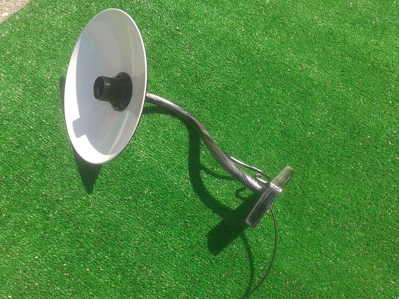 Op de afbeelding: Een witte metalen lamp met een gebogen arm en een witte kap. De lamp is aan de muur gemonteerd en heeft een zwart snoer.