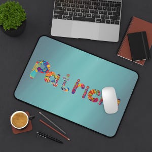 May include: A personalized mousepad with the name "Patrick" in colorful, patterned letters on a teal background. A white computer mouse rests on the pad, with a laptop and office supplies in the background.