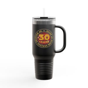 May include: Black insulated tumbler with a handle and a straw. The tumbler features a circular emblem with the text "30 YEARS OF BUILDING SUCCESS BY BRICK" in gold and red. The tumbler is designed to hold approximately 30 ounces.