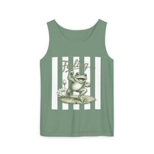 May include: A sage green tank top featuring a central graphic of a frog standing on a lily pad next to a lotus flower. Above the frog, the word "Feeling..." is printed in a cursive script. The design is set against a background of vertical white stripes.