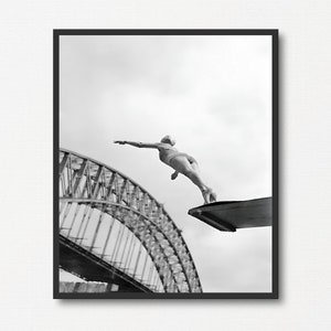 Könnte beinhalten: Ein Schwarzweißfoto einer Person, die von einer Plattform ins Wasser springt. Im Hintergrund ist die Sydney Harbour Bridge zu sehen.