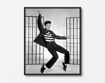 May include: Black and white photograph of a man in a striped shirt and jacket, posing in front of a barred window. He is wearing jeans and black shoes.