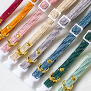 Può includere: Un set di nove collari per cani colorati con dettagli dorati e fibbie bianche. I collari sono realizzati in tessuto intrecciato con un leggero luccichio.