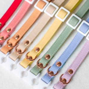 Può includere: Un set di dieci collari per cani colorati con fibbie in plastica bianca e anelli in metallo color oro rosa. I collari sono realizzati in tessuto morbido e testurizzato e sono disponibili in una varietà di colori, tra cui rosso, rosa, arancione, giallo, verde, blu e viola.