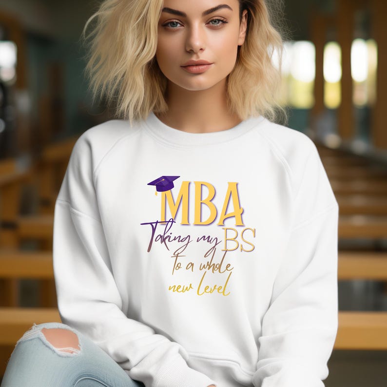May include: White sweatshirt with the text "MBA Taking my BS to a whole new level" in gold and purple. The design includes a graduation cap. The sweatshirt is a casual style.
