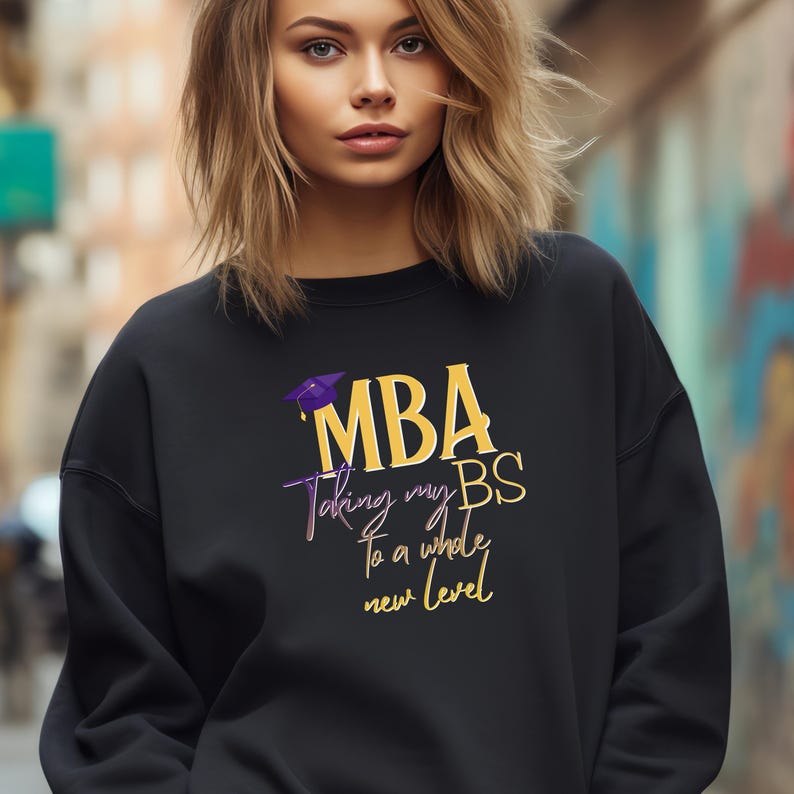 May include: Black sweatshirt with the text "MBA Taking my BS to a whole new level" in gold and purple. The design includes a graduation cap graphic. The sweatshirt is a casual garment.