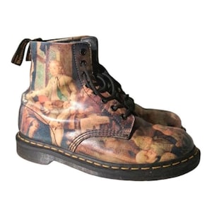 Puede incluir: Botines con diseño pintado. Las botas tienen suela negra, cordones negros y una lengüeta en la parte trasera. El diseño pintado representa una escena con figuras de estilo clásico, con tonos marrones, beige y azules.