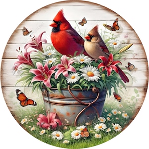 May include: A round wooden sign with a whitewashed background features a rustic metal bucket overflowing with pink lilies and white daisies. Two red cardinals perch on the rim of the bucket, while butterflies flutter around the flowers.