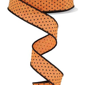 May include: Orange and black polka dot ribbon with a black edge. The ribbon is made of a textured fabric.