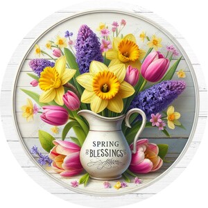 May include: A white pitcher with the text "Spring Blessings" filled with a bouquet of yellow daffodils, pink tulips, and purple hyacinths. The flowers are arranged on a white wooden background.