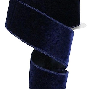 May include: A spool of deep navy blue velvet ribbon with a soft, plush texture and finished edges. The ribbon is wound around a white plastic core, displaying a rich, dark colour and a consistent, smooth surface throughout the entire length.