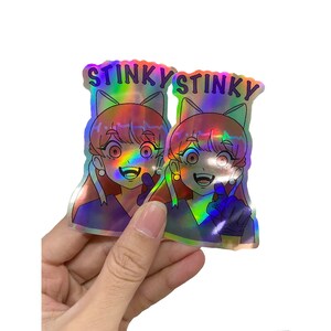 May include: Two iridescent holographic stickers featuring a cartoon character with pink hair, blue eyes, and a mischievous grin. The stickers say "Stinky" in a purple font.