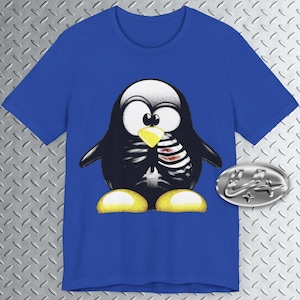 以下が含まれることがあります： ロイヤルブルーのTシャツに、漫画のペンギンのグラフィックがプリントされています。ペンギンは黒で、目は白く、くちばしは黄色です。ペンギンの胸には骨格のデザインが施され、右のひれには骨を持っています。