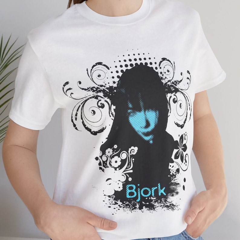 May include: White t-shirt with a black and white graphic print of a woman's face with blue eyes and the word "Bjork" printed below.