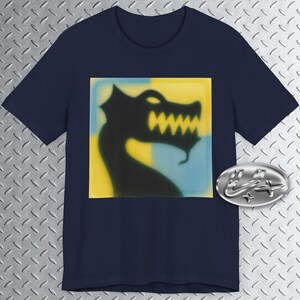 May include: Navy blue t-shirt featuring a black dragon silhouette on a yellow and blue square. The dragon has sharp teeth and a curved neck. A silver emblem is on the lower right. The shirt is a casual wear item.