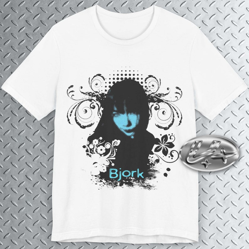 May include: White t-shirt with a black and white graphic design featuring a woman's face with blue eyes and a floral design. The text "Bjork" is printed in blue on the shirt.
