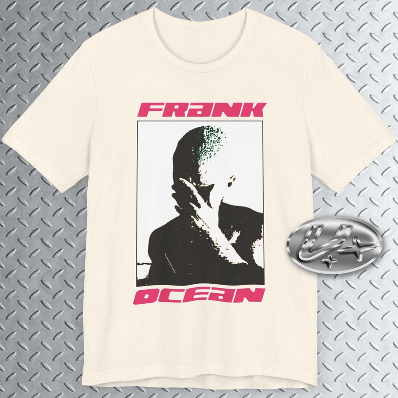 May include: A cream-coloured t-shirt with a black and white image of a person's face with the text "FRANK OCEAN" in pink letters.