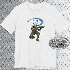 May include: White t-shirt with a blue and green graphic of a video game character holding a weapon. The character is standing in front of a blue ring with the number "2" in the center.