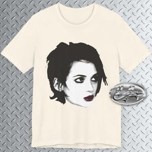Pode incluir: Uma camiseta branca com uma imagem em preto e branco de uma mulher com cabelo curto e escuro. A mulher est&aacute; olhando para a direita e tem olhos escuros e l&aacute;bios vermelhos.
