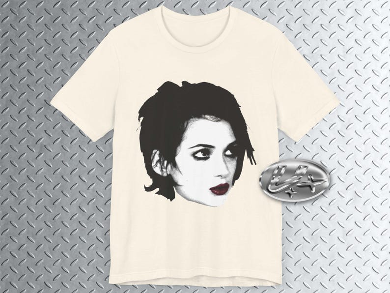 Pode incluir: Uma camiseta branca com uma imagem em preto e branco de uma mulher com cabelo curto e escuro. A mulher est&aacute; olhando para a direita e tem olhos escuros e l&aacute;bios vermelhos.