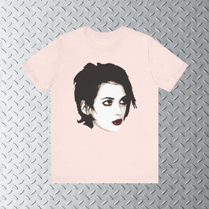 Pode incluir: Uma camiseta rosa com uma imagem em preto e branco de uma mulher com cabelo preto curto. A mulher est&aacute; olhando para a direita e tem olhos escuros e l&aacute;bios vermelhos.