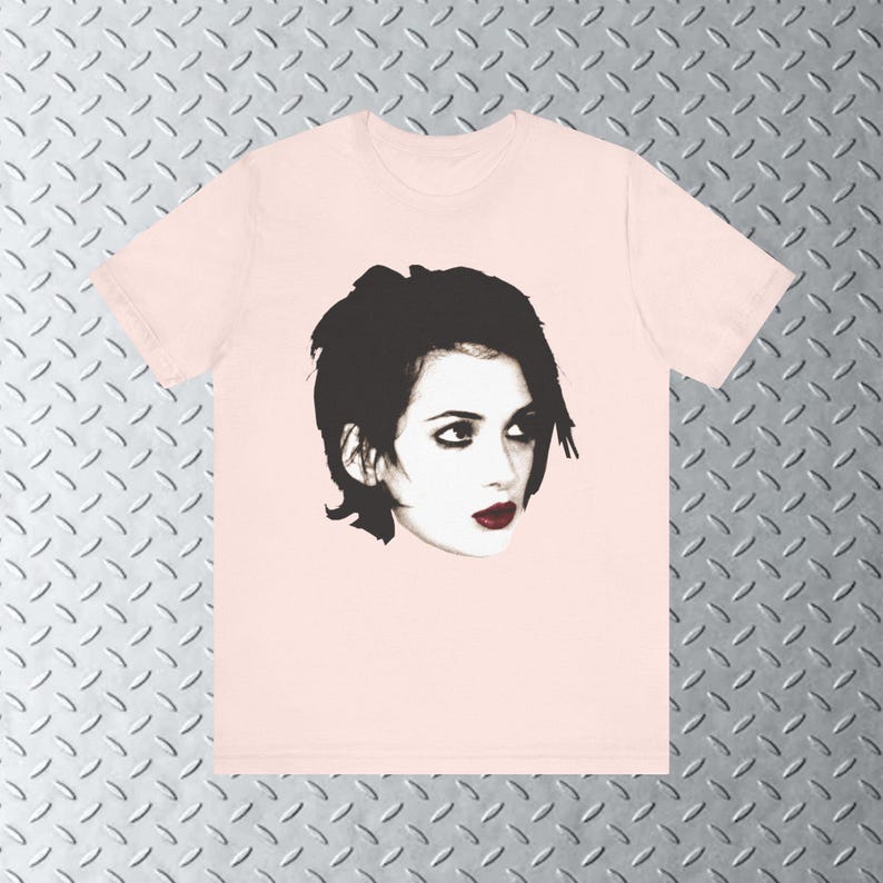 Pode incluir: Uma camiseta rosa com uma imagem em preto e branco de uma mulher com cabelo preto curto. A mulher est&aacute; olhando para a direita e tem olhos escuros e l&aacute;bios vermelhos.