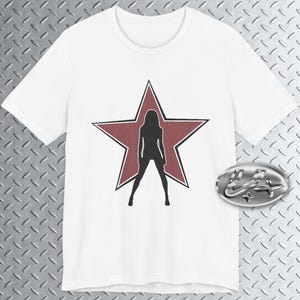 May include: White t-shirt with a silhouette of a person inside a red star. The graphic is centered on the shirt. The shirt is made of a soft material. A silver emblem is in the lower right corner.