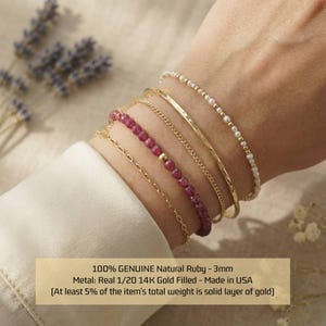 May include: A collection of gold-filled bracelets and a ruby bead bracelet are displayed on a wrist. The bracelets include a hammered gold bangle, a delicate chain, and a pearl beaded bracelet. The text on the image reads: 100% GENUINE Natural Ruby - 3mm.