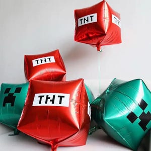 May include: A collection of square-shaped foil balloons featuring red TNT blocks with white labels and green Creeper faces with black pixelated details. These metallic party decorations are designed with sharp corners and a glossy finish.