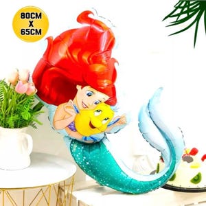 May include: A mermaid-shaped foil balloon, featuring a red-haired mermaid and a yellow fish. The balloon is teal, blue, and yellow, and measures 80cm x 65cm.