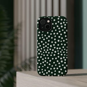 K&ouml;nnte beinhalten: Dunkelgr&uuml;ne Handyh&uuml;lle mit wei&szlig;em Polka-Dot-Muster. Die H&uuml;lle hat einen schwarzen Kameraobjektiv-Ausschnitt und eine glatte, gl&auml;nzende Oberfl&auml;che. Die Handyh&uuml;lle liegt auf einer hellen Holzoberfl&auml;che.