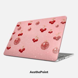 Puede incluir: Funda rosa para portátil con un estampado de cerezas rojas y adornos de bolas de discoteca. El diseño incluye destellos blancos en forma de estrella. El texto "AesthePoint" está en la parte inferior del portátil.