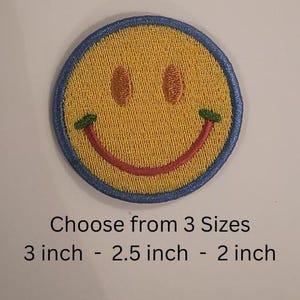 Puede incluir: Parche bordado de carita sonriente amarilla con sonrisa roja, ojos marrones y detalles verdes. El parche tiene un borde azul y está disponible en 3 tamaños: 7,6 cm, 6,4 cm y 5,1 cm.